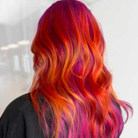 Vibrant hair with pink, orange, and red shades, styled in soft waves.