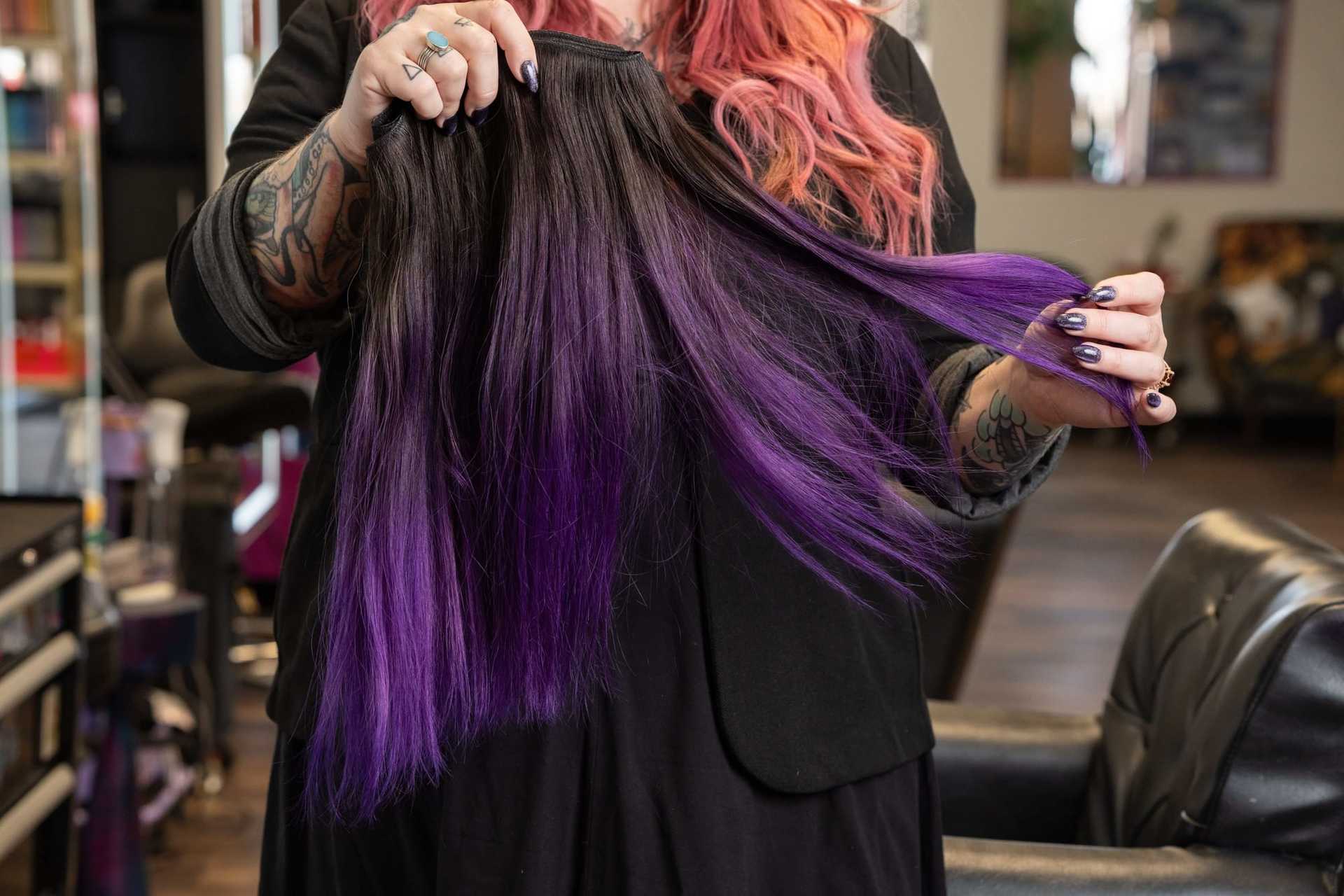 Person holding long, black and purple hair extensions in a salon setting.